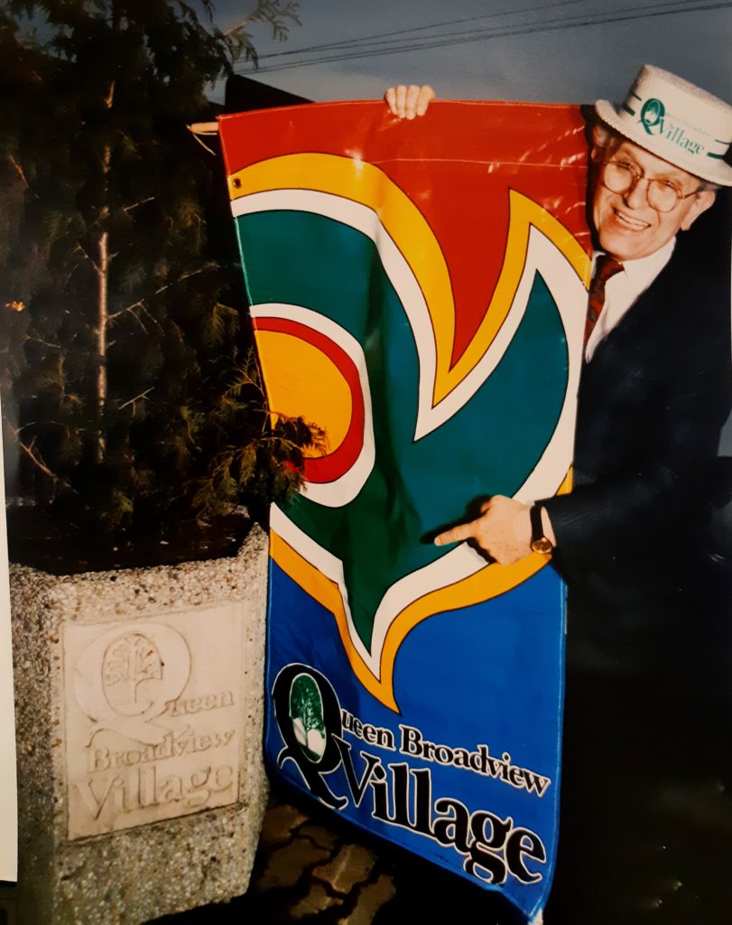Albert Edelstein, former Chair of the Queen-Broadview Village BIA (now Riverside BIA) in a 1993 photo showing off the BIA's new banner and planters improving the streetscape on Queen East (Photo by Jack Kohane)